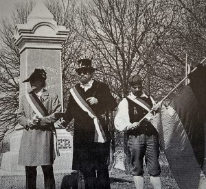Historische schwarzweiß Fotografie dreier Personen, die – erkennbar an den Heckerhüten und Fahnen – der badischen Revolution anhängen. Sie stehen an der Hecker-Gedenkstätte.