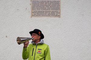 Mann mit Heckerhut und Regenjacke vom Schwarzwaldverein, der in ein metallenes Signalhorn bläst.