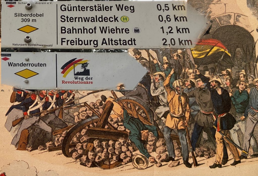 Wegweiser-Schild mit der Aufschrift „Weg der Revolutionäre“ am Wegweiserstandort Siblerdobel (309 m).
