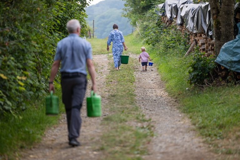 Ein älterer Mann, eine Frau und ein Kind tragen Gießkannen und Eimer auf einem Schotterweg. Das Foto ist im Naturschutzgebiet Küssenberg aufgenommen worden.